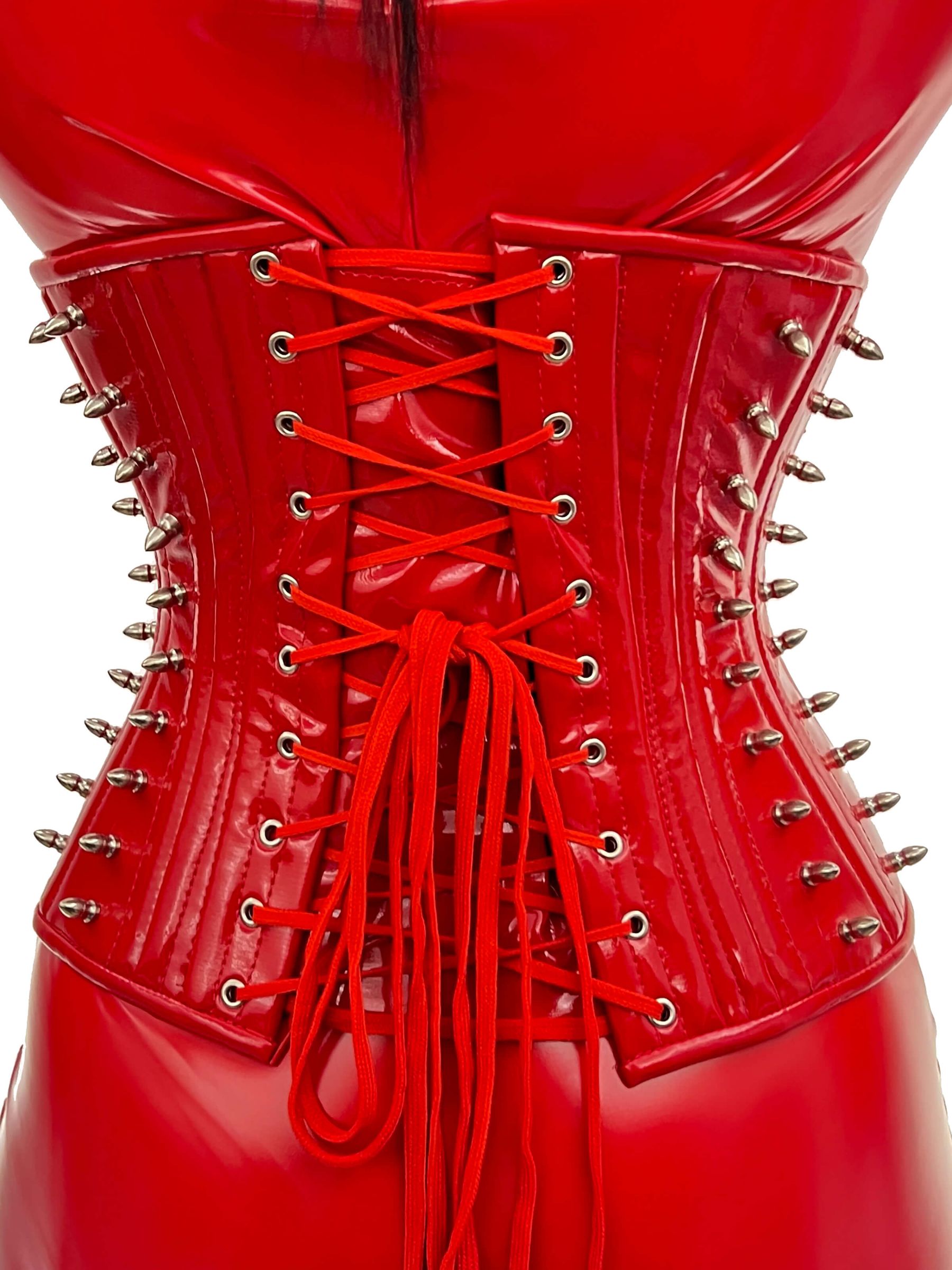Rückansicht eines roten Lackkorsetts mit Schnürung und silbernen Spikes, getragen über glänzendem Lackoutfit
