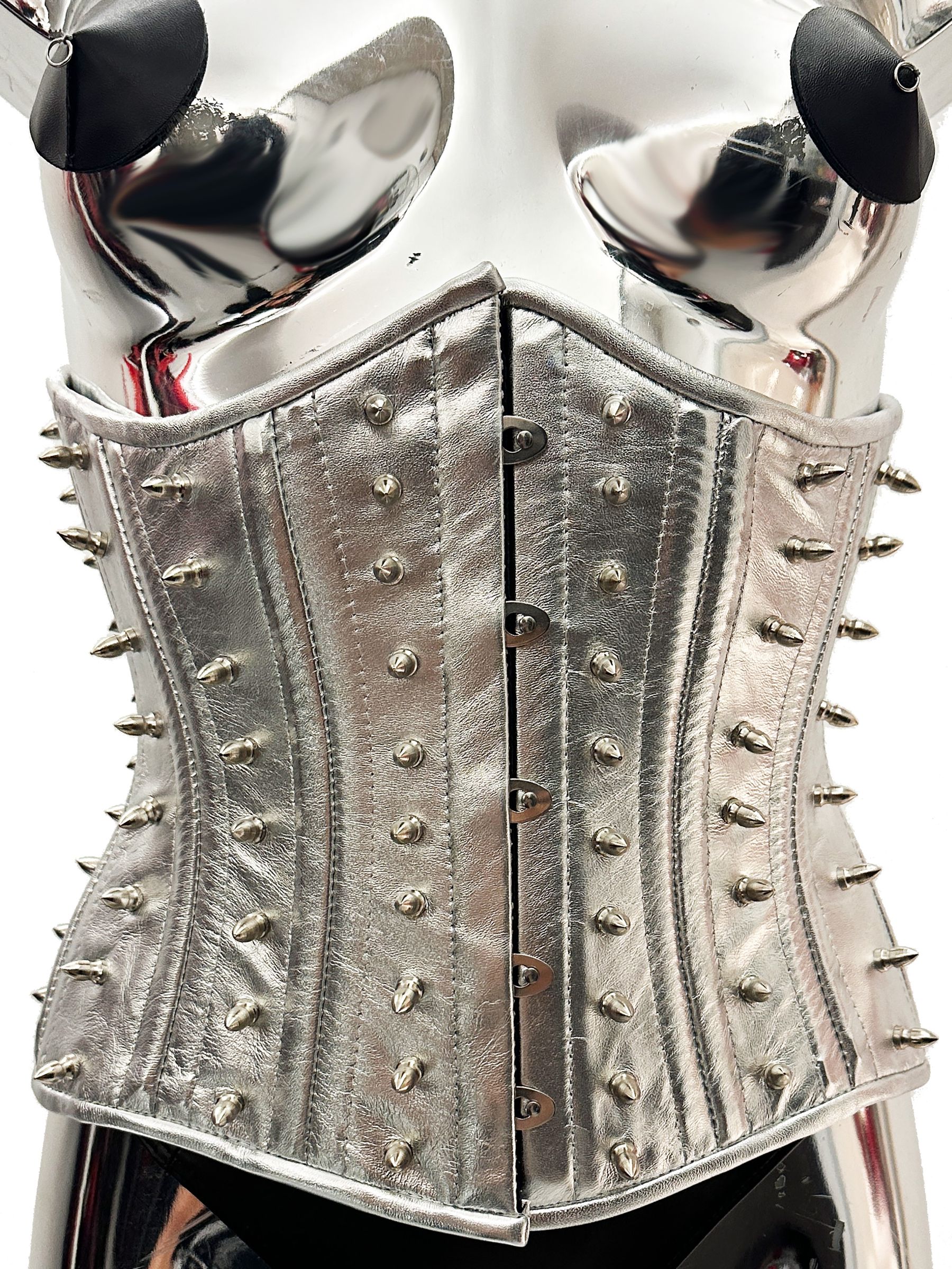 Silbernes Echtleder-Korsett mit Metallspikes, taillenformend, auf glänzendem Schaufenster-Torso präsentiert.