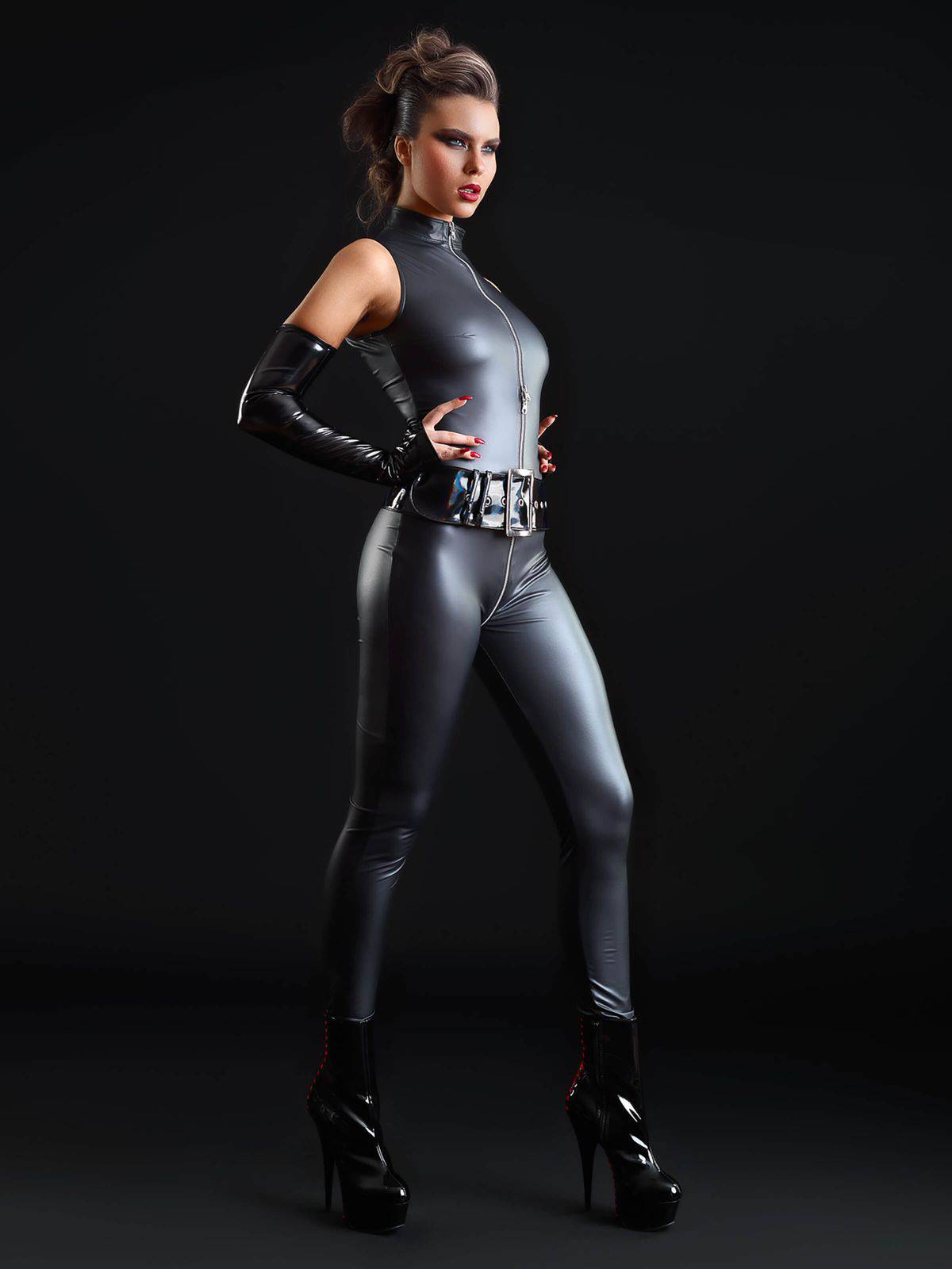 Frau seitlich im Wetlook Catsuit mit glänzendem Lackgürtel, langen Handschuhen und High Heels vor dunklem Hintergrund.